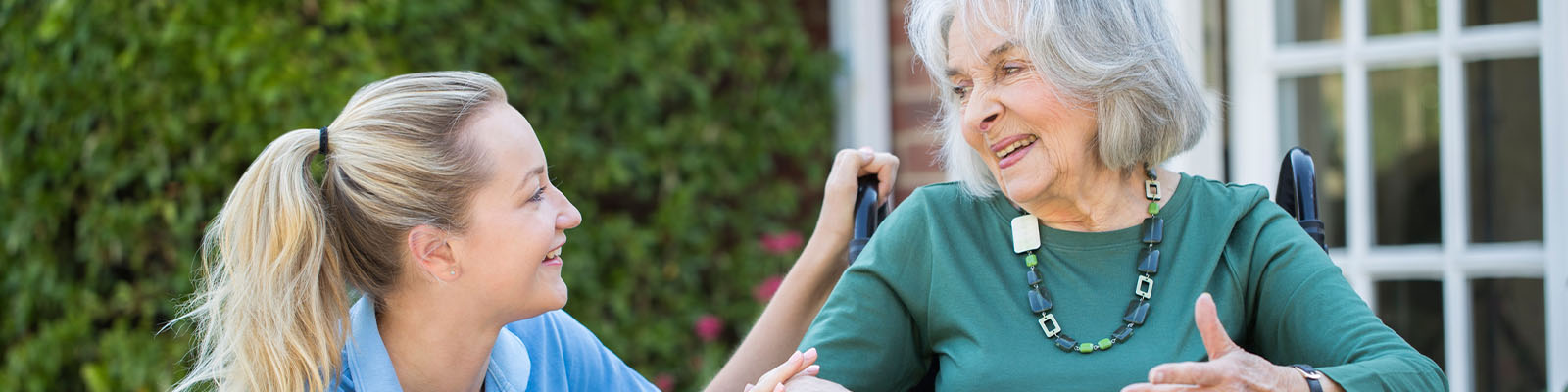 A senior living employee crouched down checking on a senior woman sitting in a wheelchair