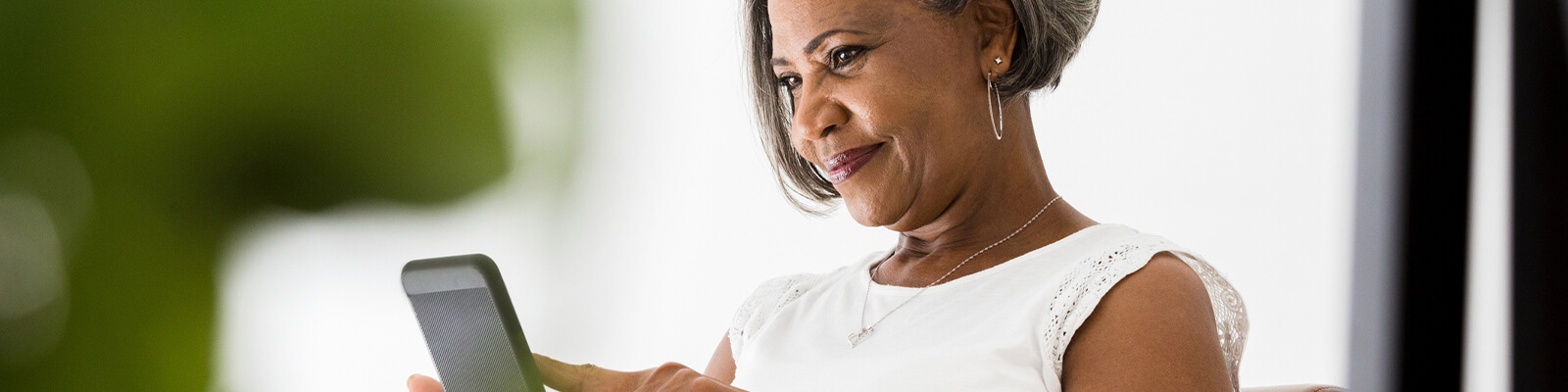 A senior woman wearing a white shirt smiling while scrolling on her smartphone