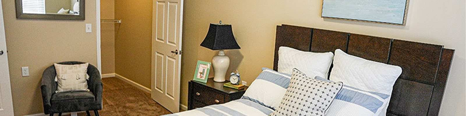 A senior living apartment at Traditions at Reagan Park with a bed, side table, and small chair