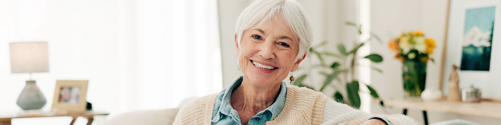 A senior woman smiling while sitting on a tan couch in a living room