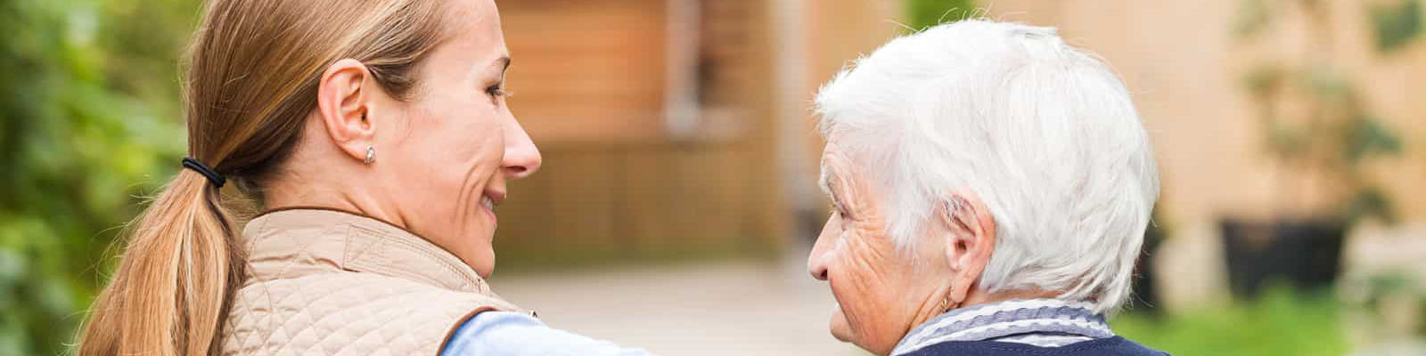 A memory care employee smiling looking over at a senior woman as they walk outdoors