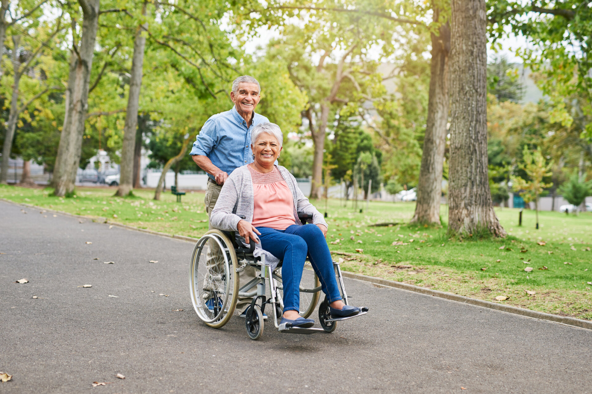 A senior man pushing his wife in a wheelchair on a walking path