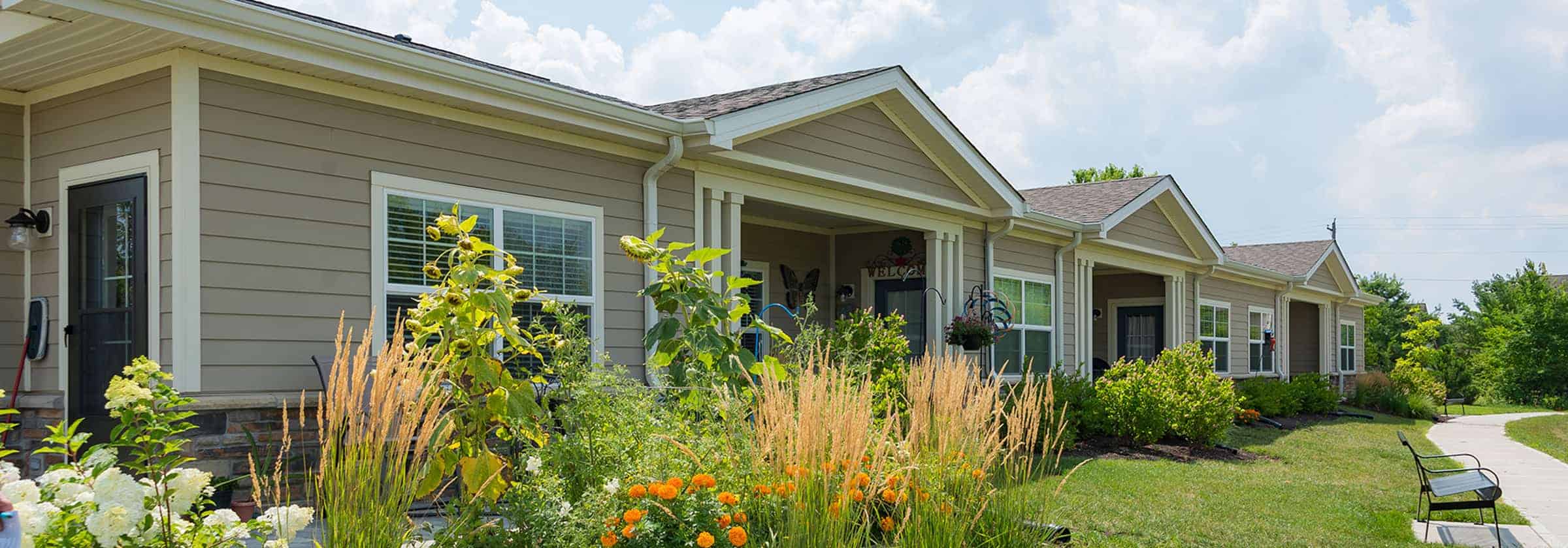 Brown independent living garden homes with white windows and green plants in flowerbeds outside